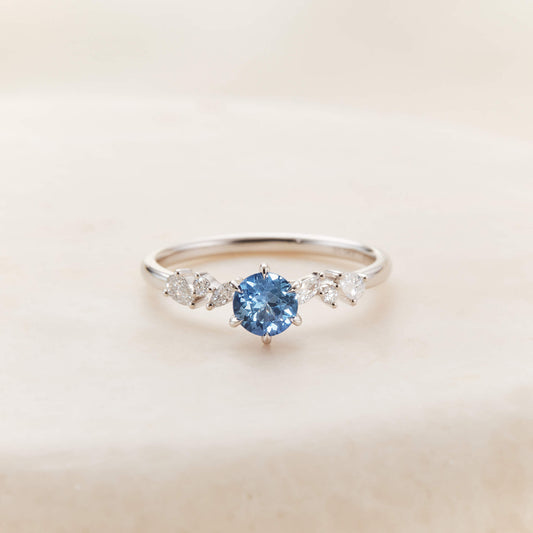 A close-up product photograph displays a delicate 14k White Gold ring centered against a textured, light beige stone surface.