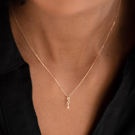 Close-up of a woman wearing the Key Charm 14k Gold pendant on a delicate gold chain with a black top