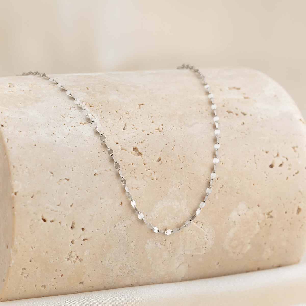 Silver chain necklace on a beige stone surface