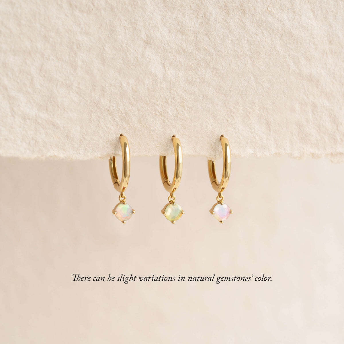 Three Gold hoop earrings with Opal gemstone, displayed against a soft cream background.