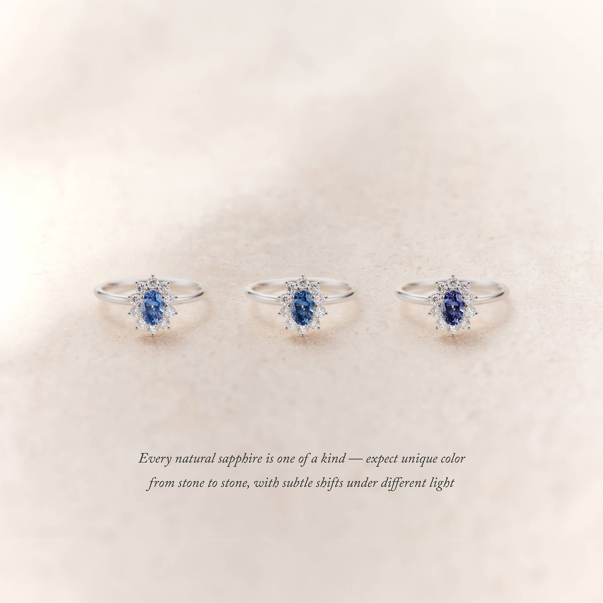 Three White Gold halo rings with oval blue sapphires surrounded by small diamonds are displayed side by side on a soft beige background.