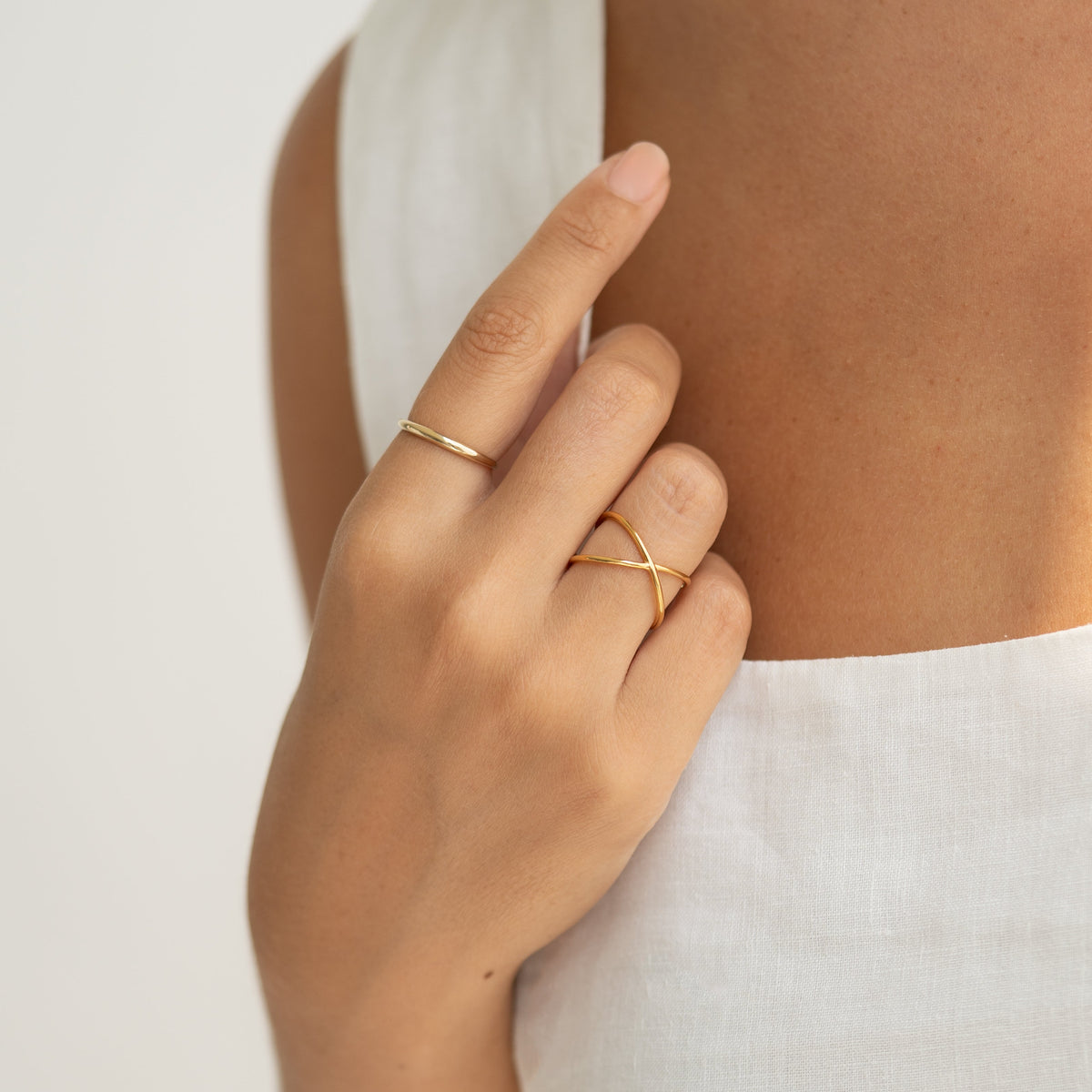 Close-up of a hand wearing the Thin Dome Ring 14k Gold - Mia styled with another gold crisscross ring on a white top