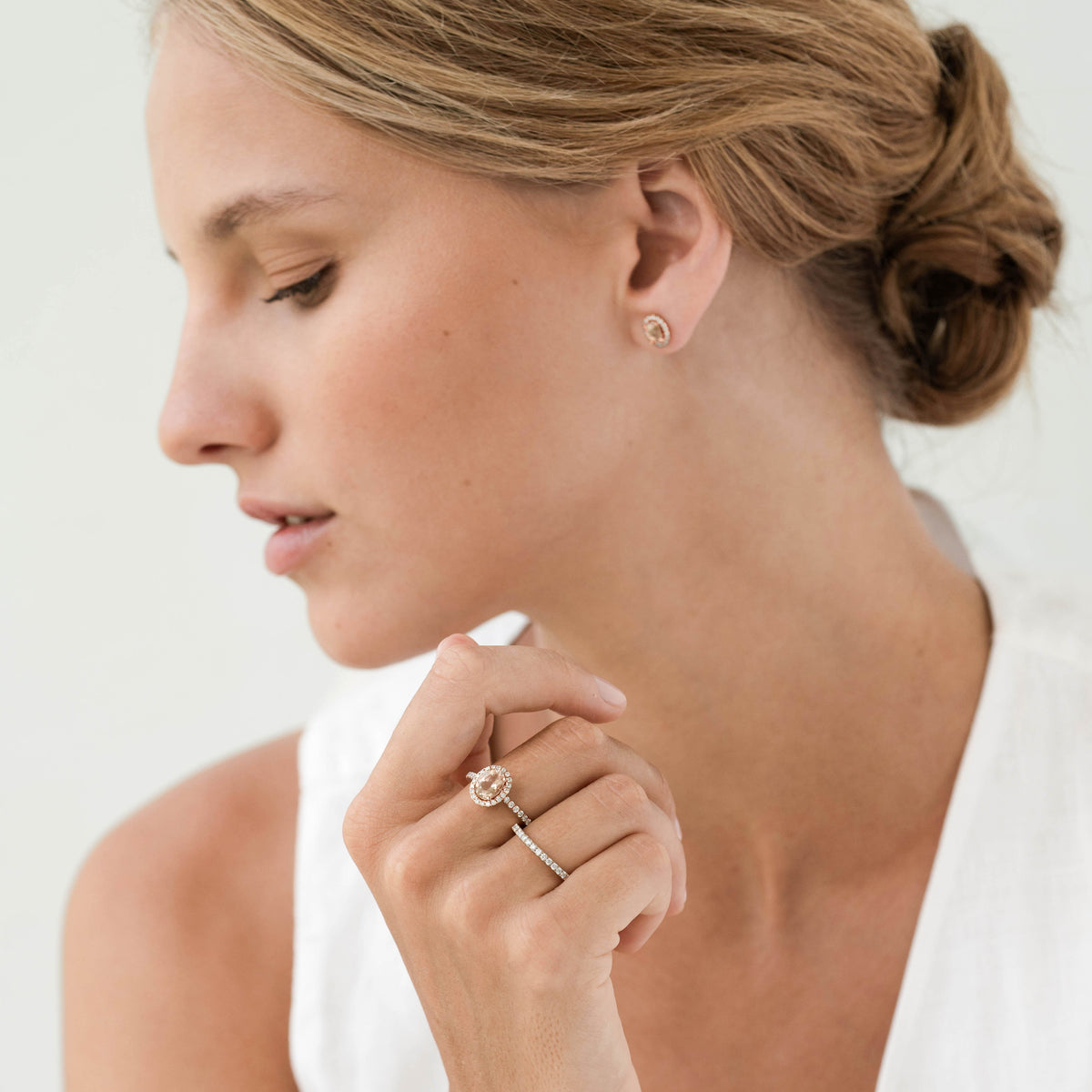 Close-up of woman wearing Oval Morganite Halo Ring Rose Gold - Suna with a white sleeveless top on a neutral background