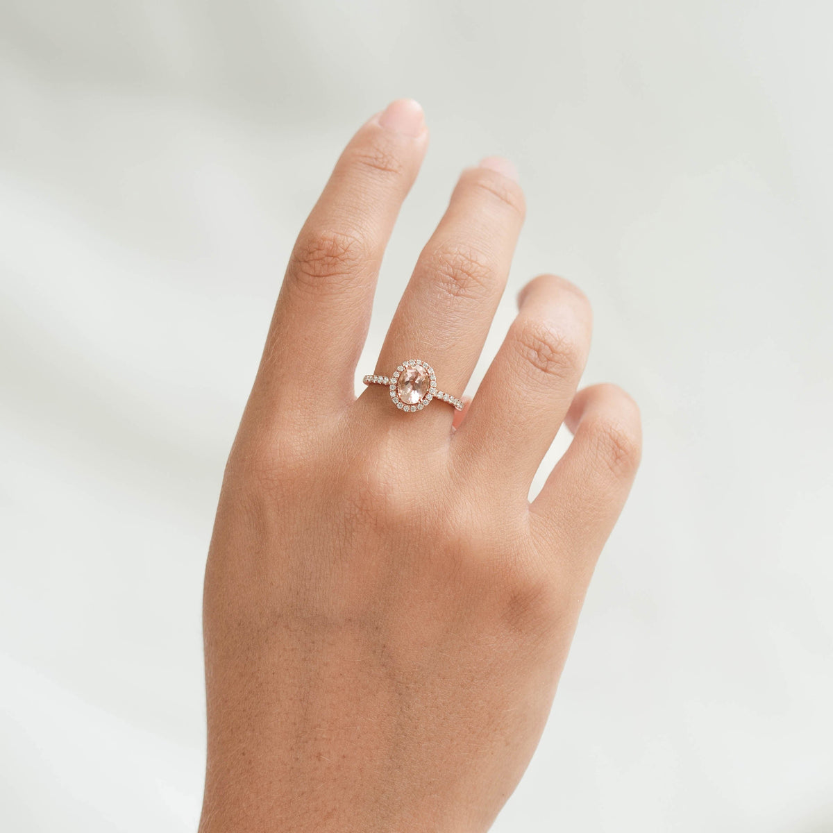Oval Morganite Halo Ring Rose Gold - Suna worn on hand with pavé diamonds and soft neutral background