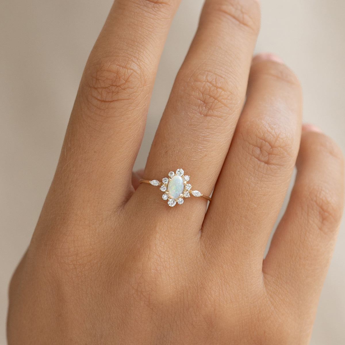 Close-up of a hand wearing Sunburst Opal Halo Ring - Solana with opal center and diamond halo in 14k yellow gold