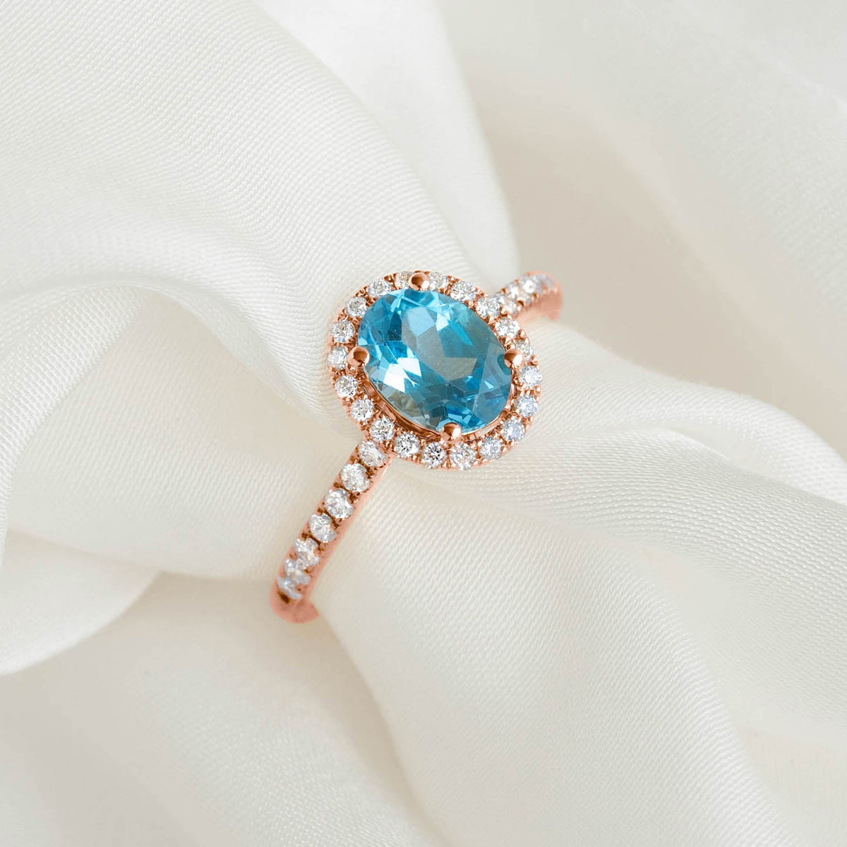 Oval Swiss Blue Topaz Halo Ring Rose Gold - Suna with pavé diamonds surrounding an oval blue topaz on white fabric