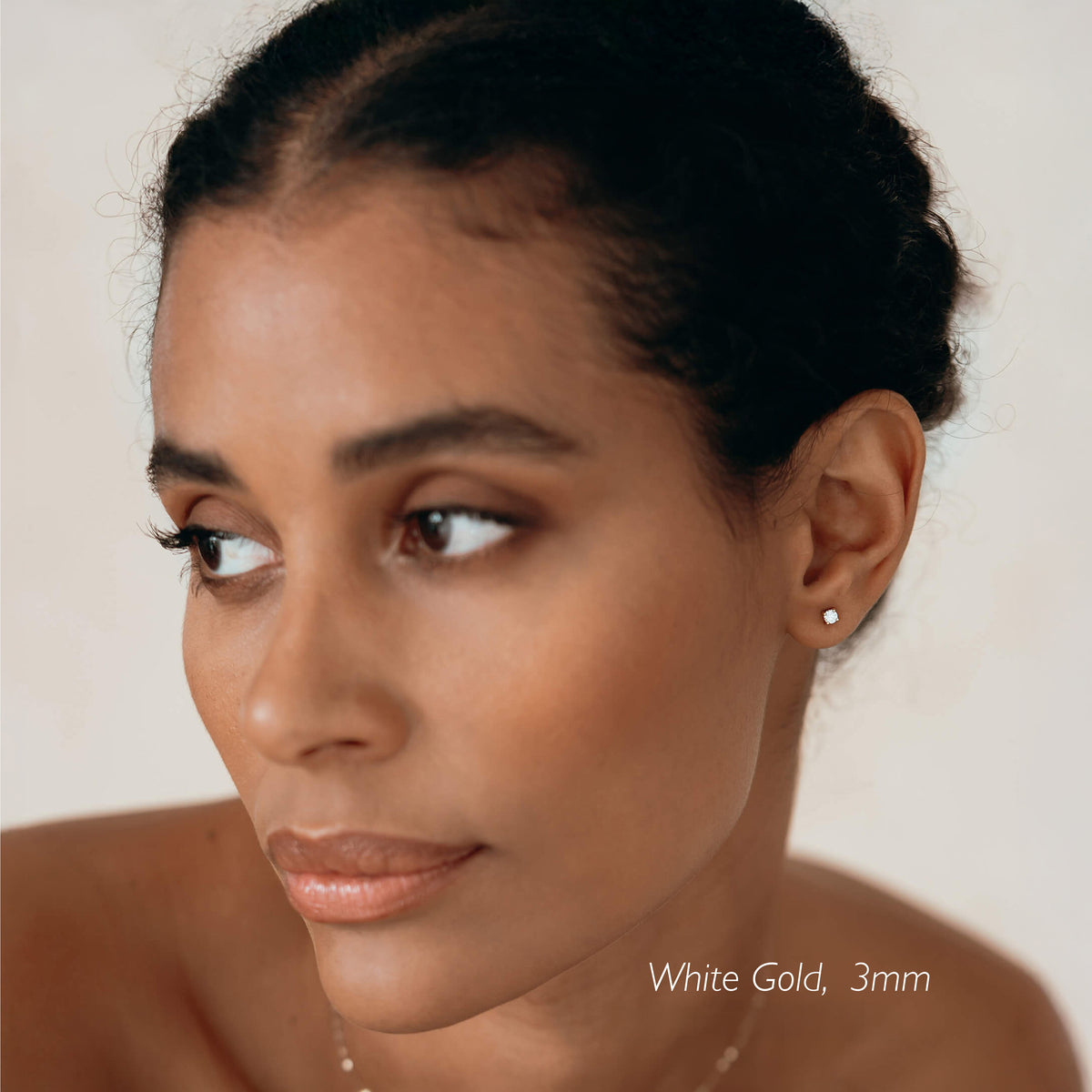 Close-up of a woman wearing 14k Yellow Gold Diamond Stud Earrings 3mm - Aria with a soft neutral background