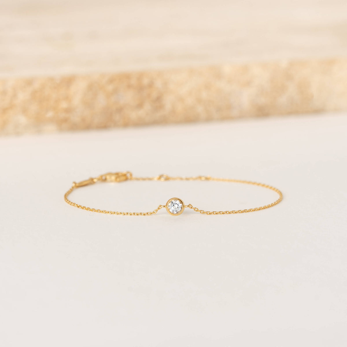 Delicate Gold Vermeil chain bracelet featuring a small round White topaz gemstone centerpiece, laid flat on a light-colored surface.