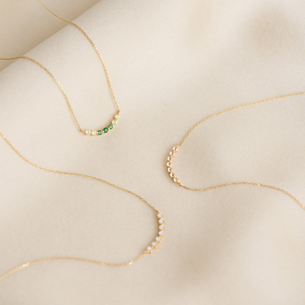 Three delicate April Birthstone Necklace 14k Gold - Diamond styles displayed on soft beige fabric background