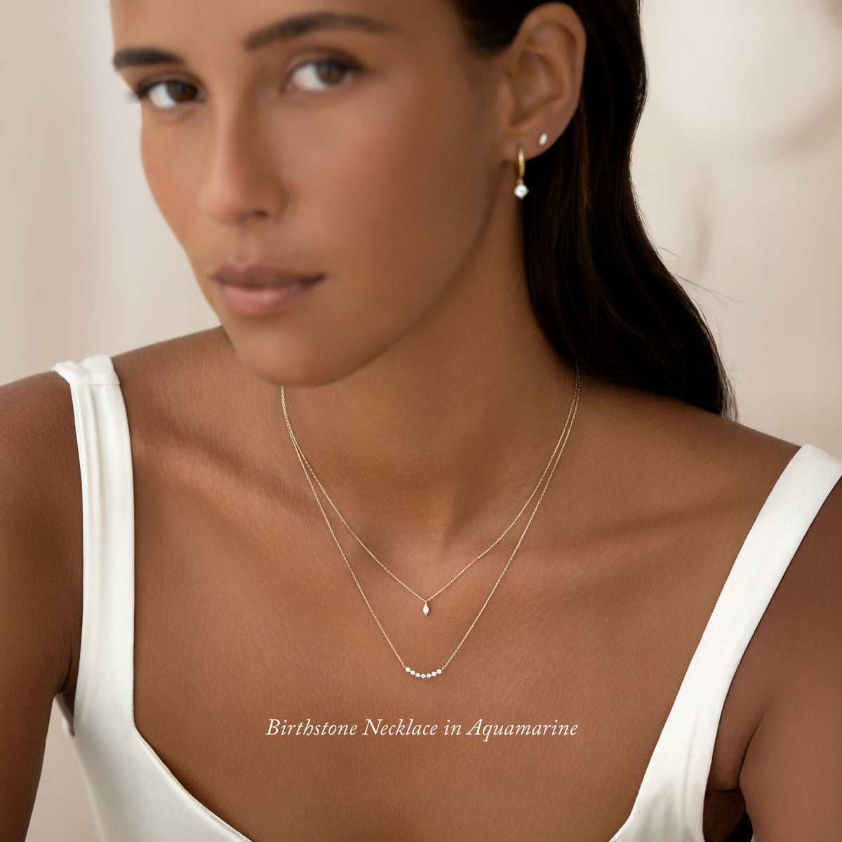 Close-up of a woman wearing the April Birthstone Necklace 14k Gold - Diamond with matching gold earrings on a neutral background