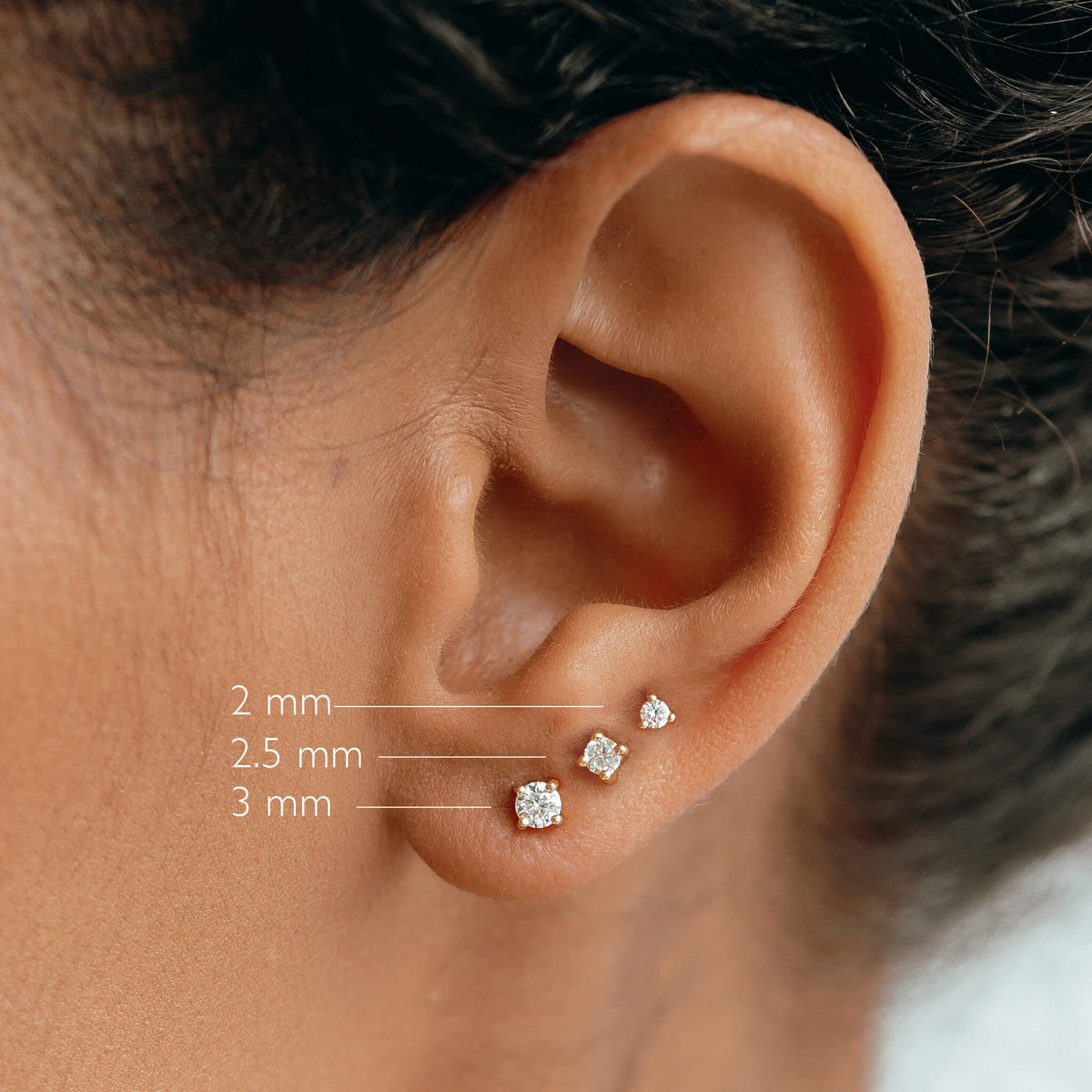 Close-up of an ear wearing 14k Yellow Gold Diamond Stud Earrings 2.5mm - Aria with size comparison labels