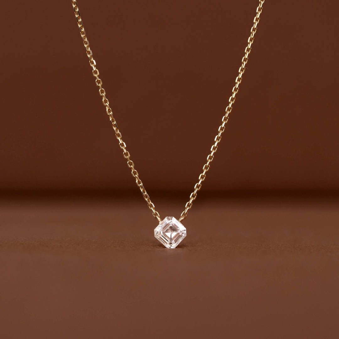 Close-up of a delicate Gold chain necklace featuring a clear asscher-cut gemstone pendant against a warm brown background.