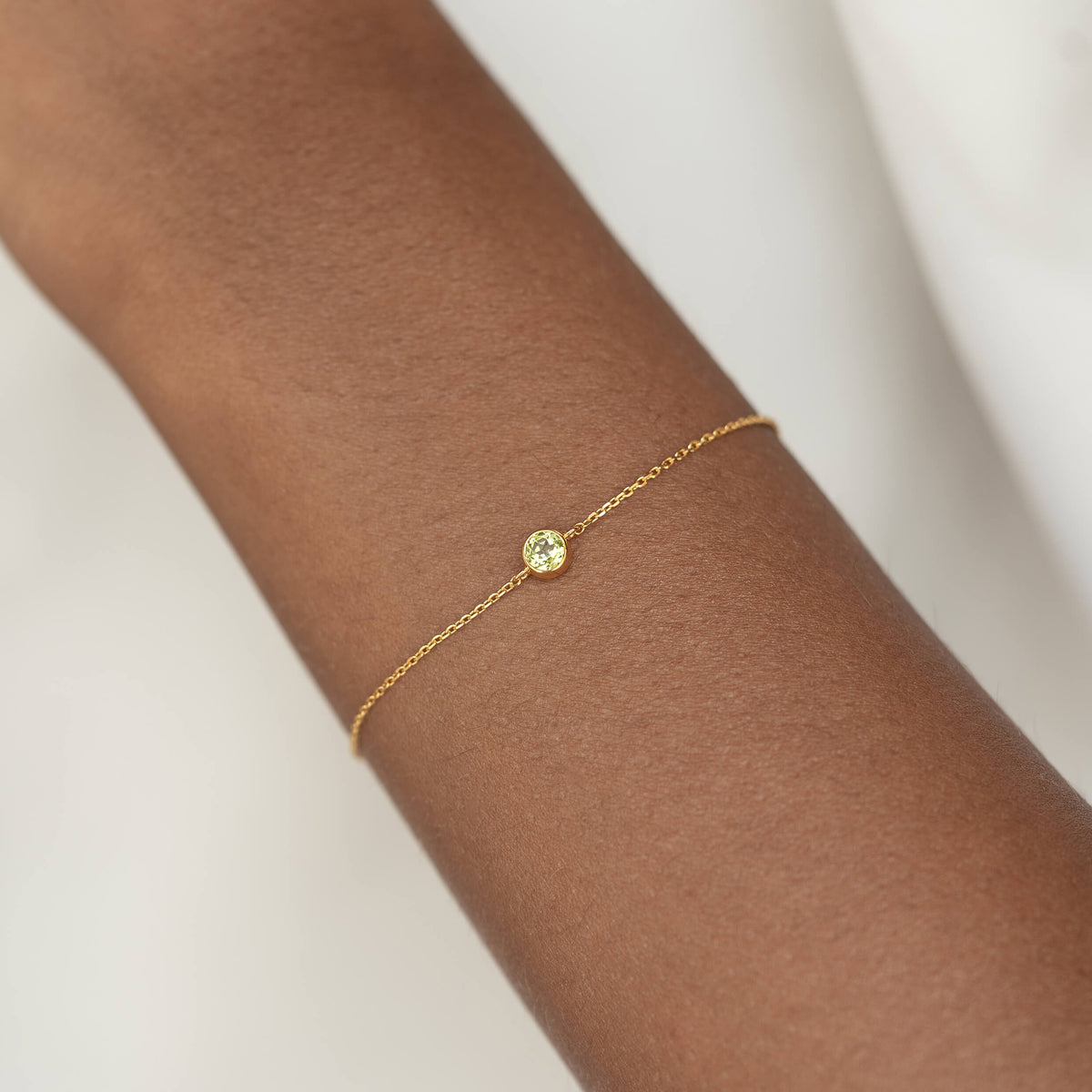 Delicate Gold Vermeil chain bracelet with a small round Peridot gemstone centerpiece, worn around a woman's wrist.