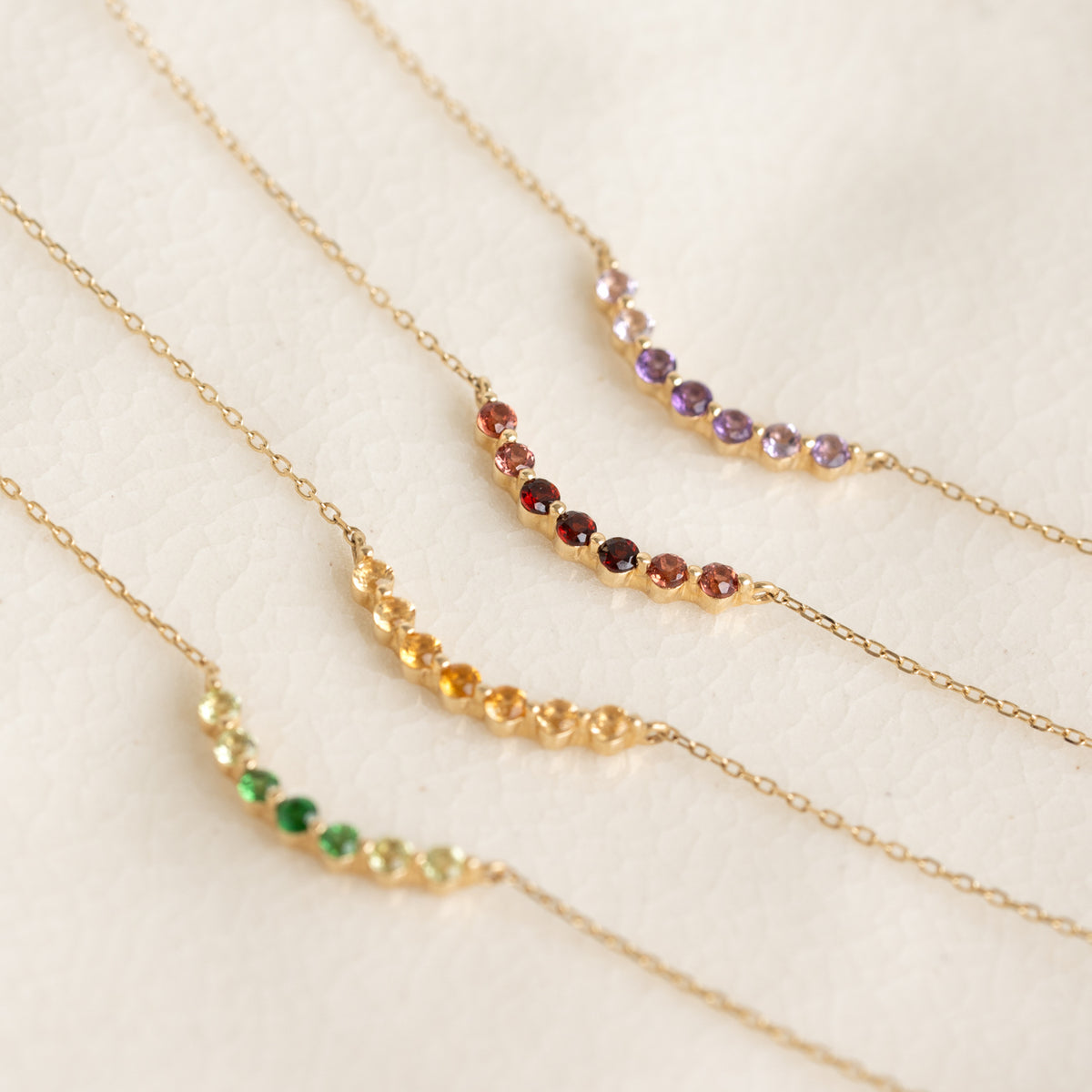 Close-up of four August Birthstone Necklace 14k Gold - Ombre Tsavorite with gradient gemstones on delicate gold chains on cream background