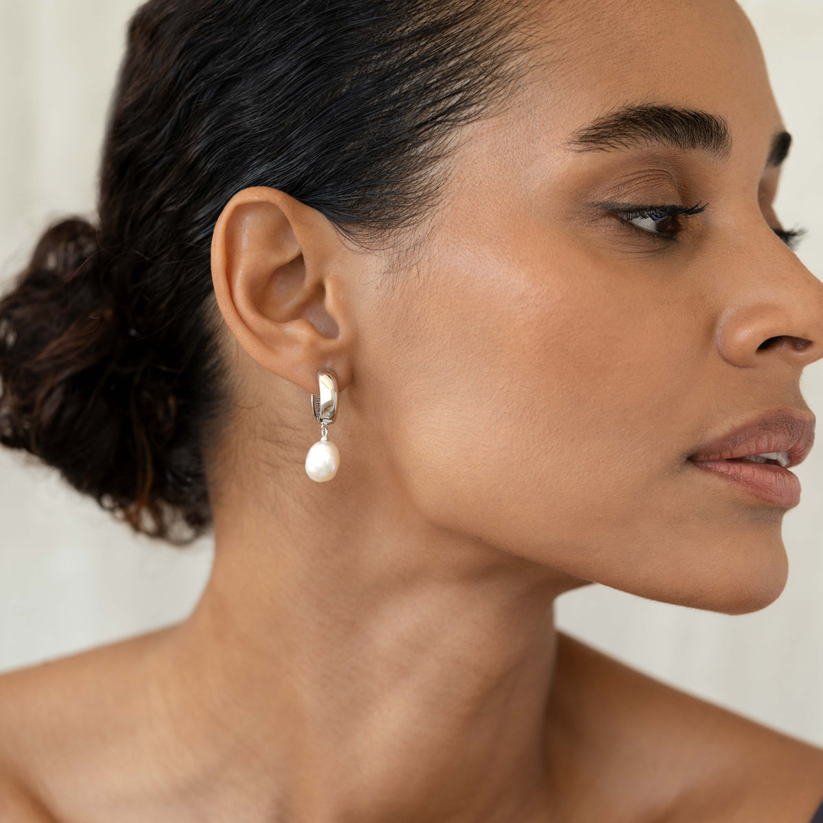 Close-up of a woman wearing Baroque Pearl Chunky Hoop Earrings Silver - Meredith with freshwater pearl drop on neutral background