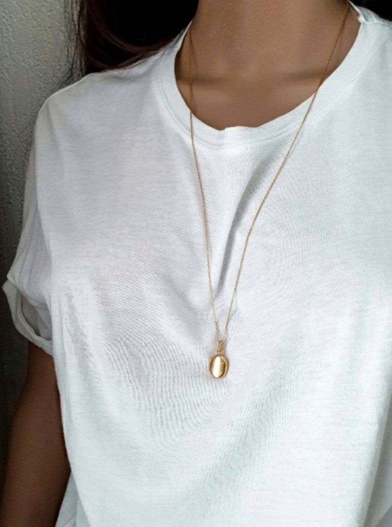 Close-up of a person wearing a plain white t-shirt and a delicate gold pendant necklace against a neutral background