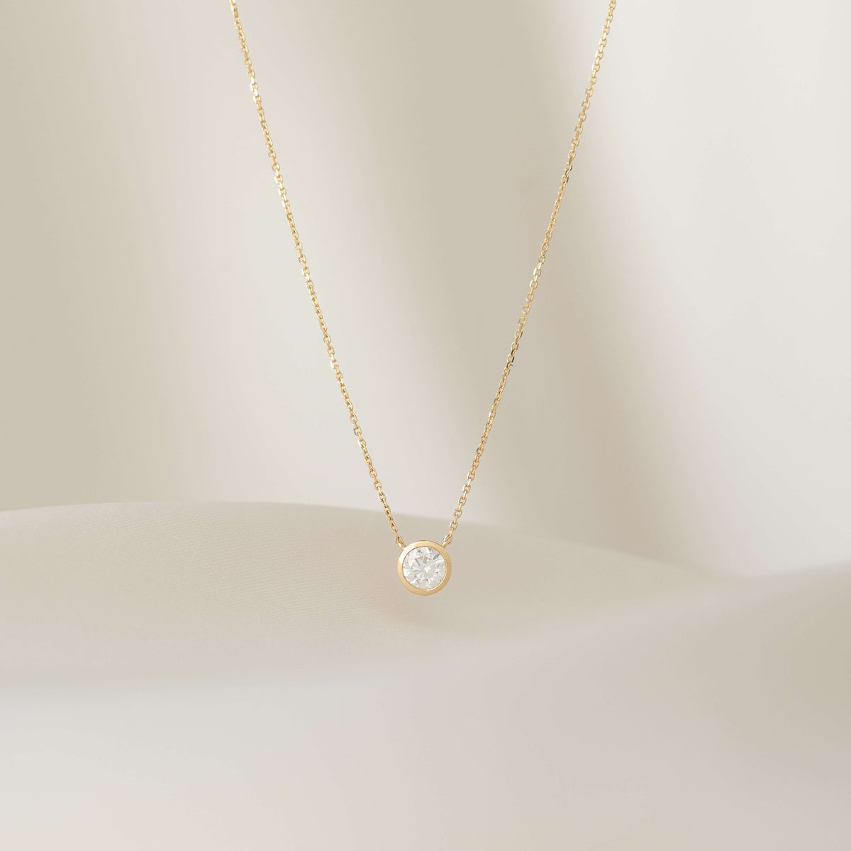 Gold necklace with a round pendant on a soft beige background