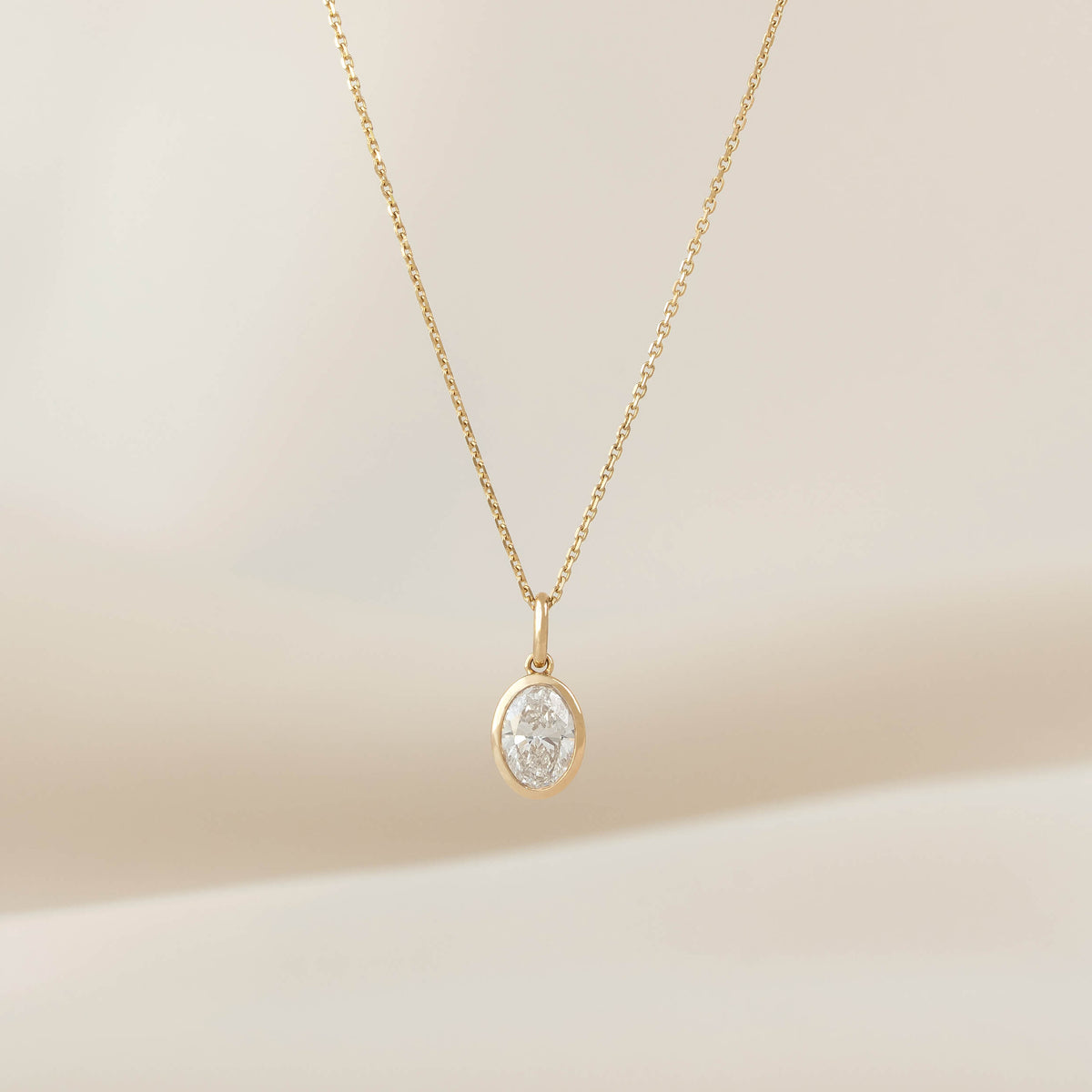 Yellow Gold necklace with a polished oval shaped pendant, displayed on a delicate chain against a soft neutral background.