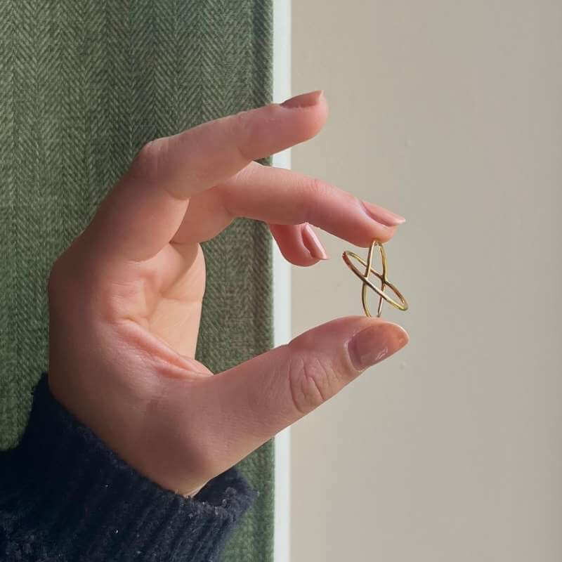Close-up of a hand holding a minimalist gold abstract geometric earring against a neutral background