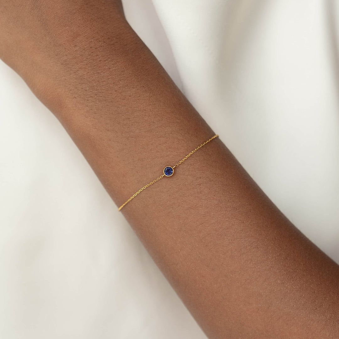 Delicate Gold Vermeil chain bracelet with a small round Cordierite gemstone centerpiece, worn around a woman's wrist.