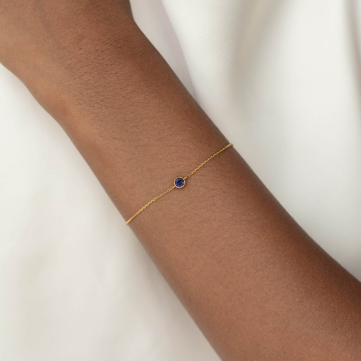 Delicate Gold Vermeil chain bracelet with a small round Cordierite gemstone centerpiece, worn around a woman's wrist.