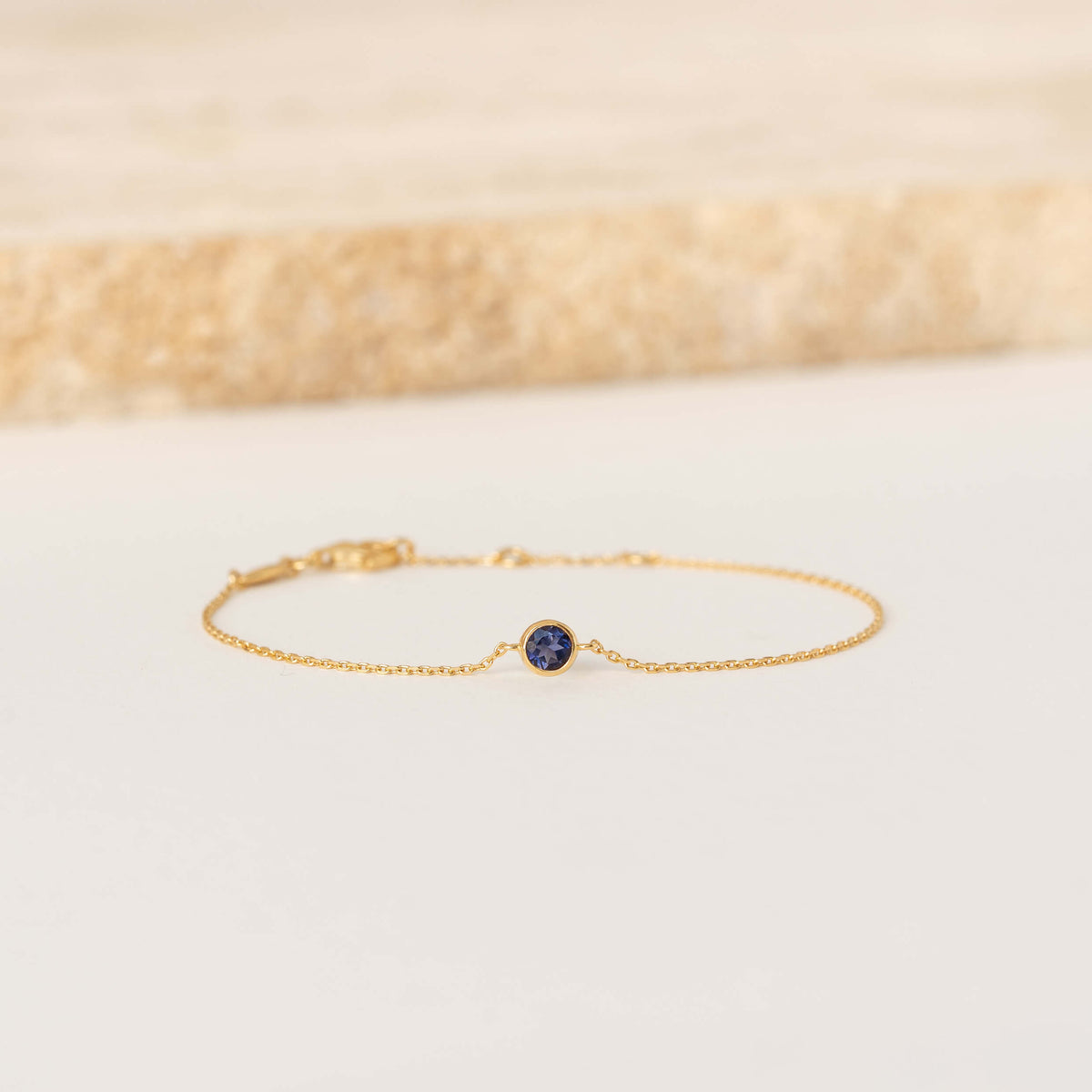 Delicate Gold Vermeil chain bracelet featuring a small round Cordierite gemstone centerpiece, laid flat on a light-colored surface.