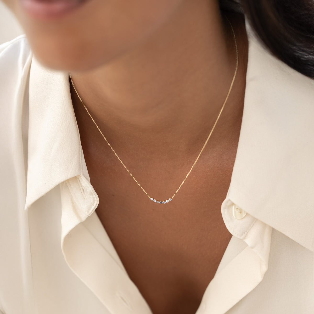 Close-up of a woman wearing the December Birthstone Necklace 14k Gold - Ombre Cordierite with a cream blouse in soft light