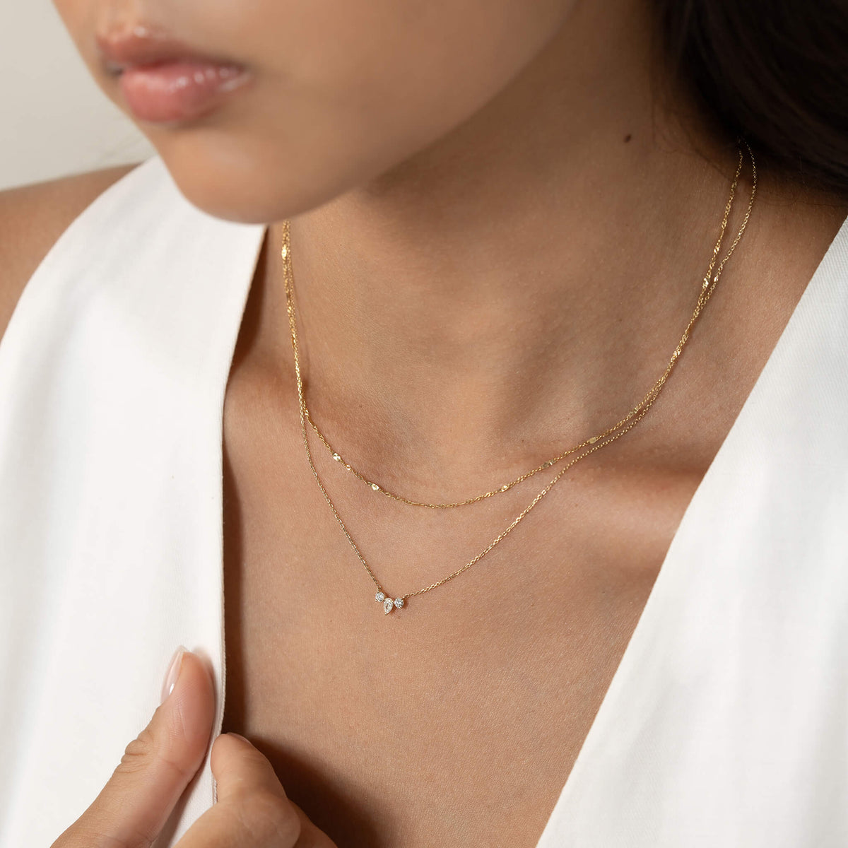 A woman wearing a white top showcases two delicate Gold necklaces with small diamond pendants. The image conveys elegance and simplicity.