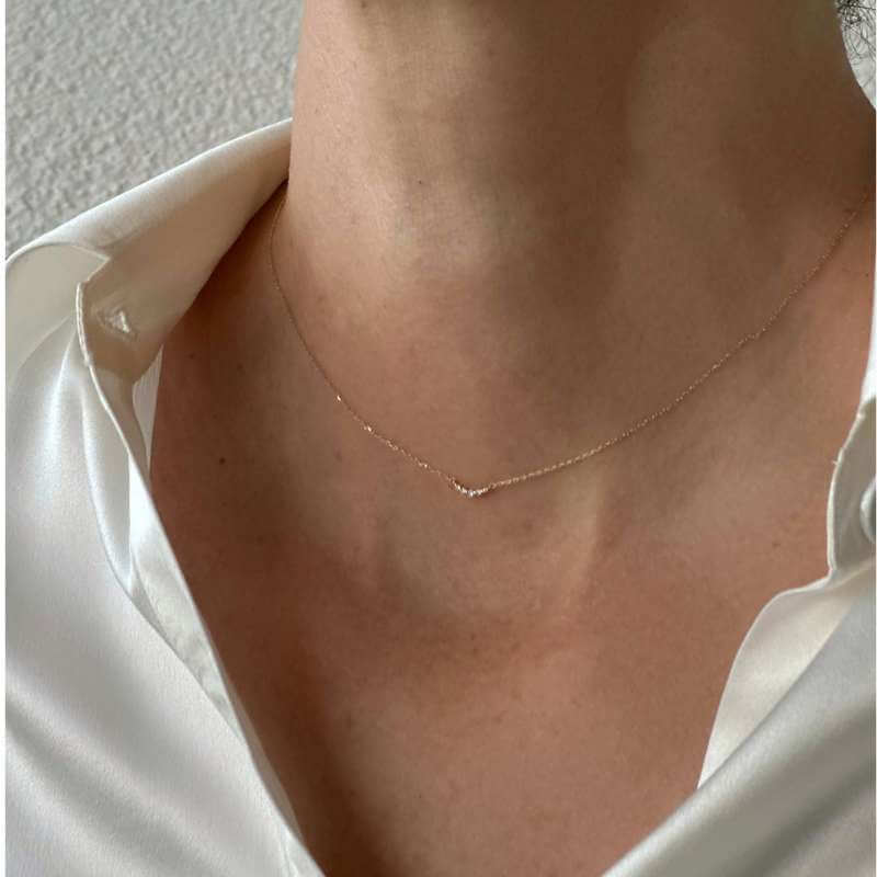 Close-up of a neck wearing a delicate thin gold chain necklace over a white shirt collar against a neutral background