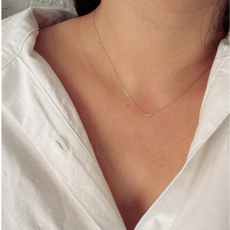 Close-up of a woman’s neck wearing a delicate gold necklace with small beads and a white button-up shirt collar