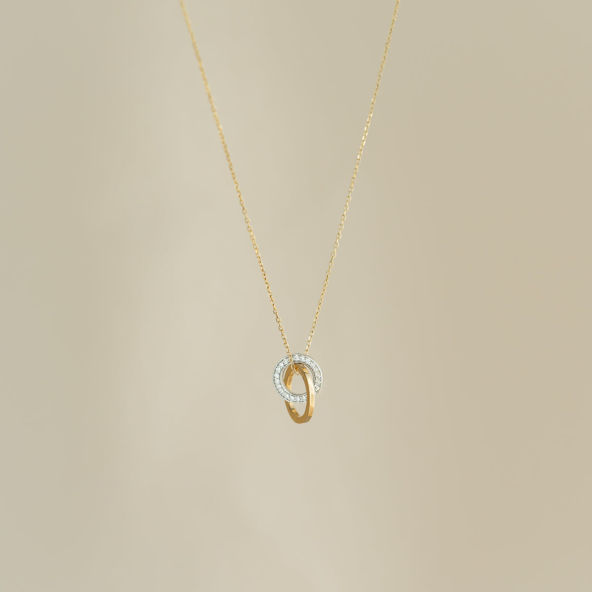 Diamond Double Circle Necklace 14k Gold - Diana with two interlocking rings, one pavé-set with diamonds, on beige background