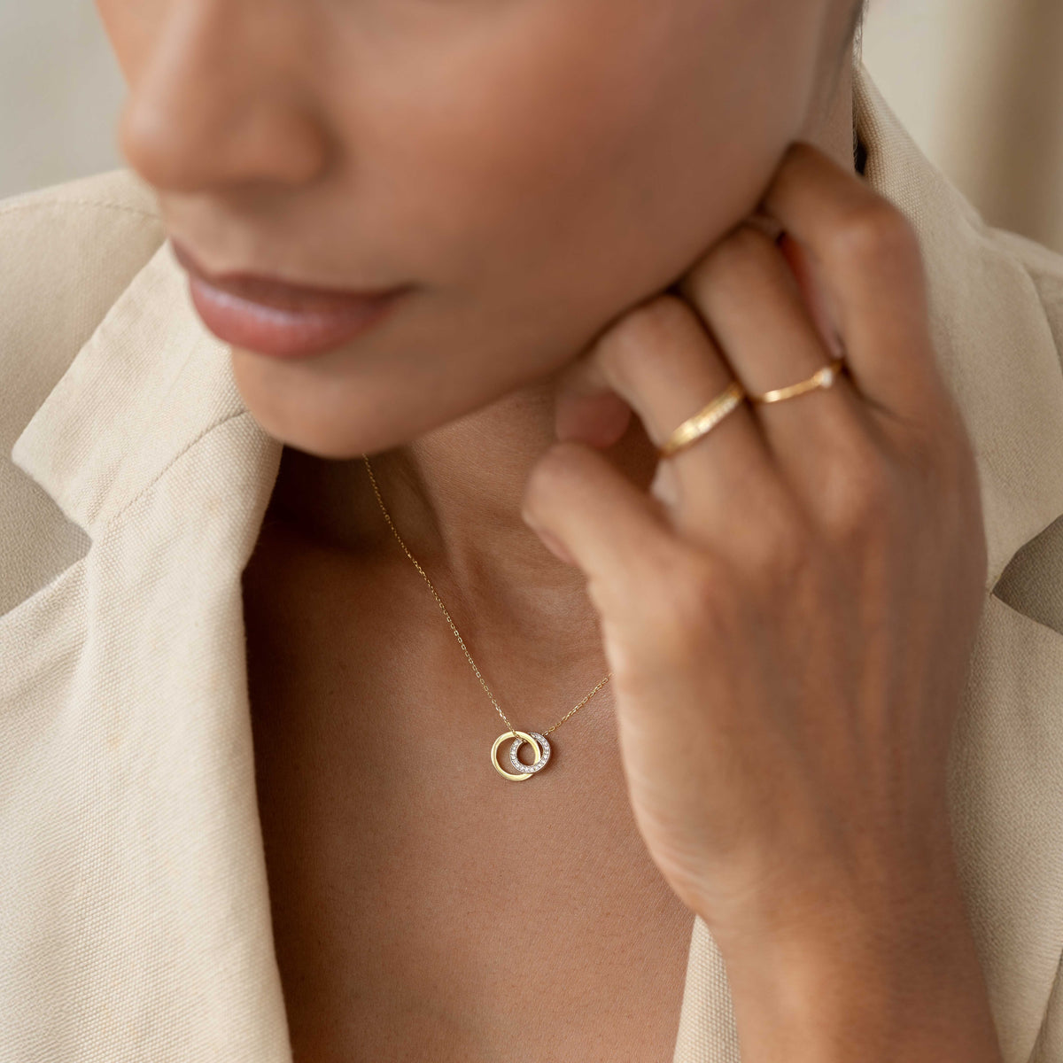 Close-up of a woman wearing the Diamond Double Circle Necklace 14k Gold - Diana with matching gold rings and beige blazer