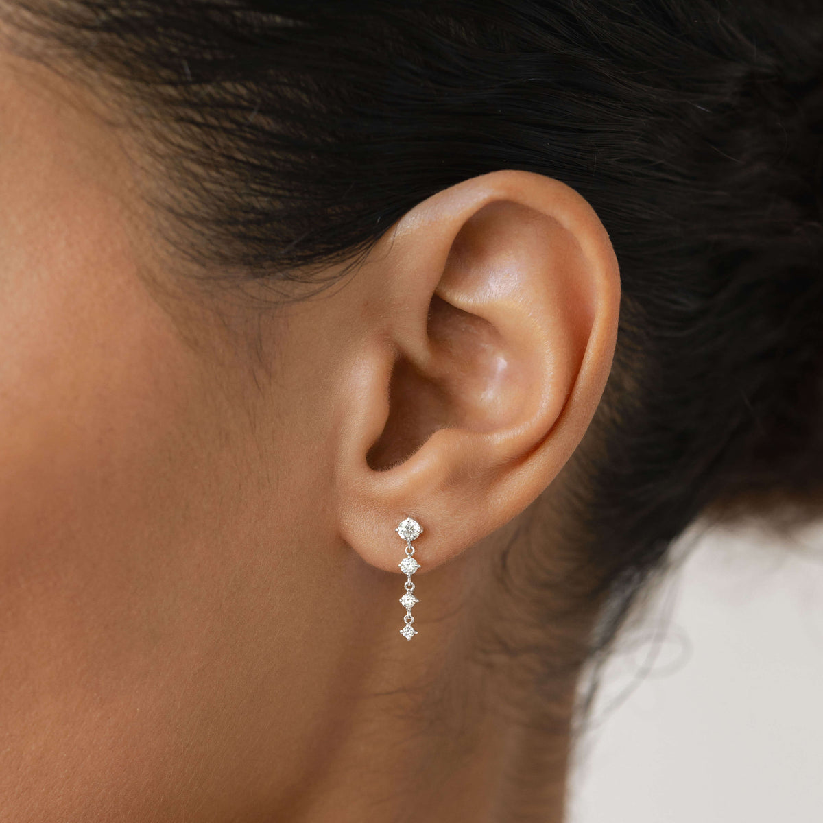 Close-up of a person’s ear wearing a delicate drop earring featuring a vertical row of small round diamonds.