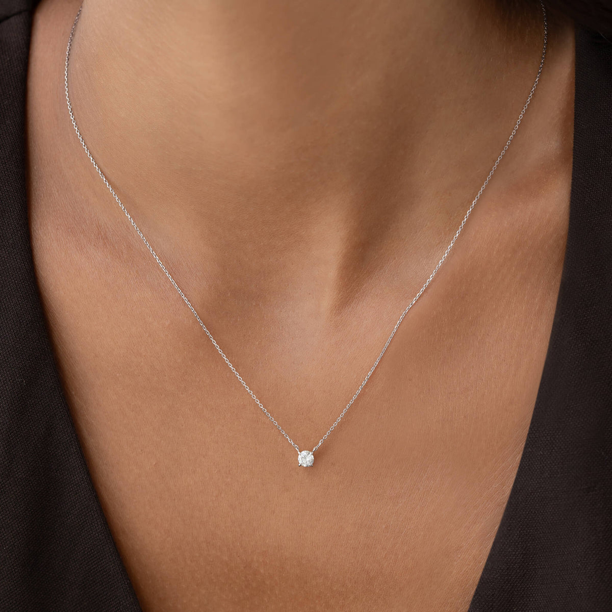 Close-up of a woman's neck wearing a delicate White Gold chain necklace with a small, round 0.25ct diamond pendant, set against a black top. Elegant and understated.
