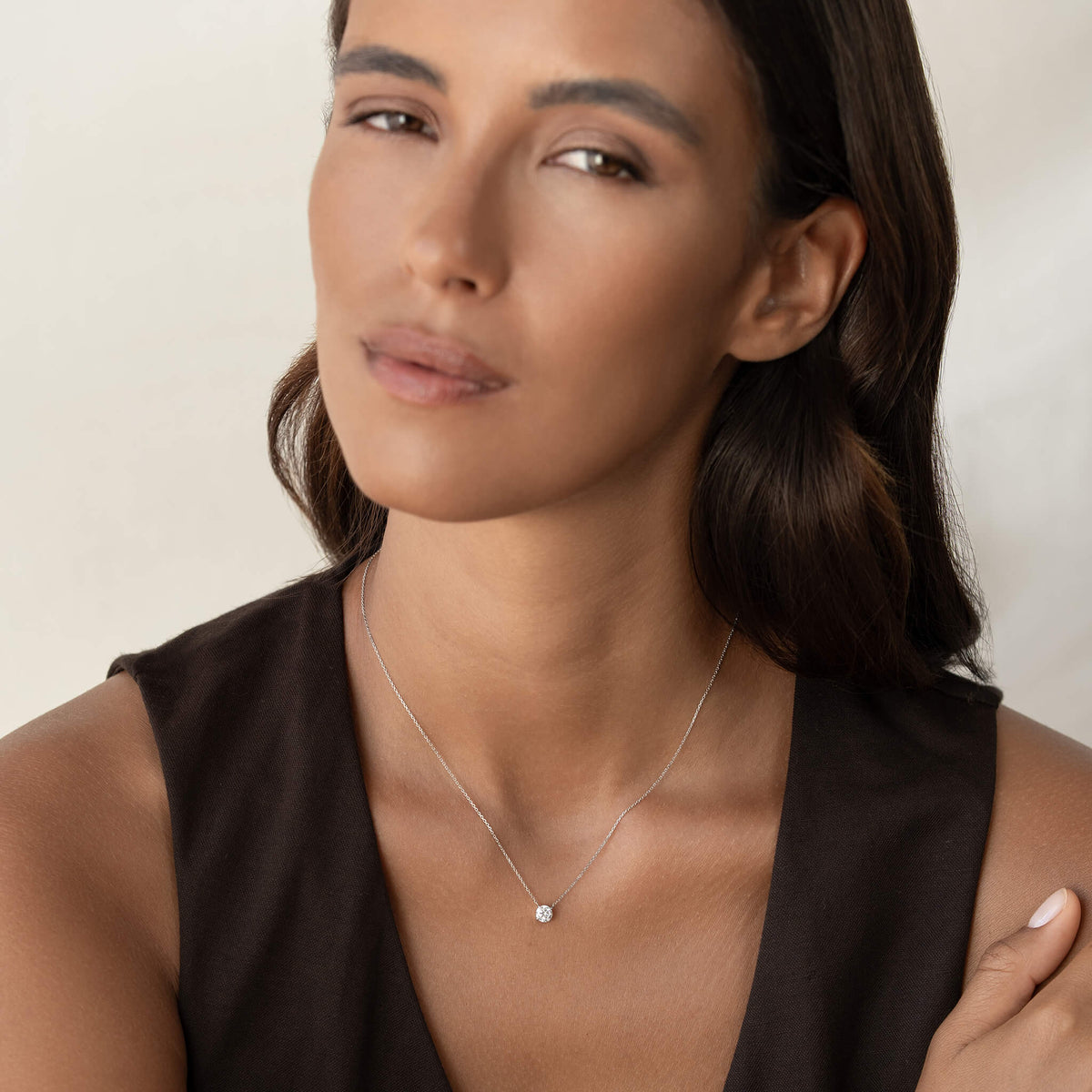 Close-up portrait of a person wearing a delicate White Gold chain necklace with a small round diamond pendant, styled with a sleeveless dark top against a neutral background.