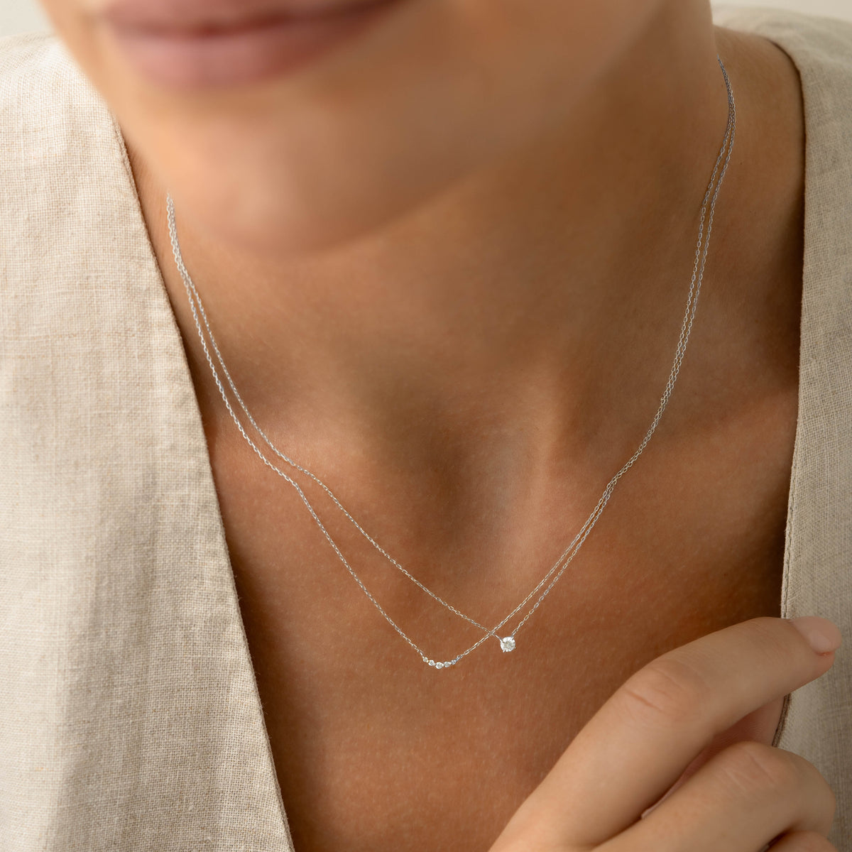 Close-up of a woman wearing Diamond Pendant Necklace White Gold - Johanne with delicate layered chains on neutral background