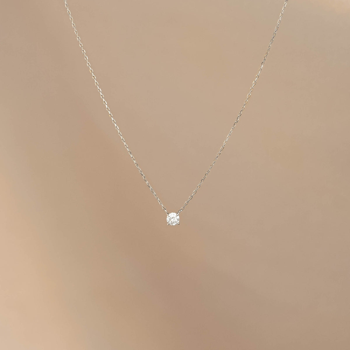 Diamond Pendant Necklace White Gold - Johanne with a single floating diamond on a delicate white gold chain on beige background