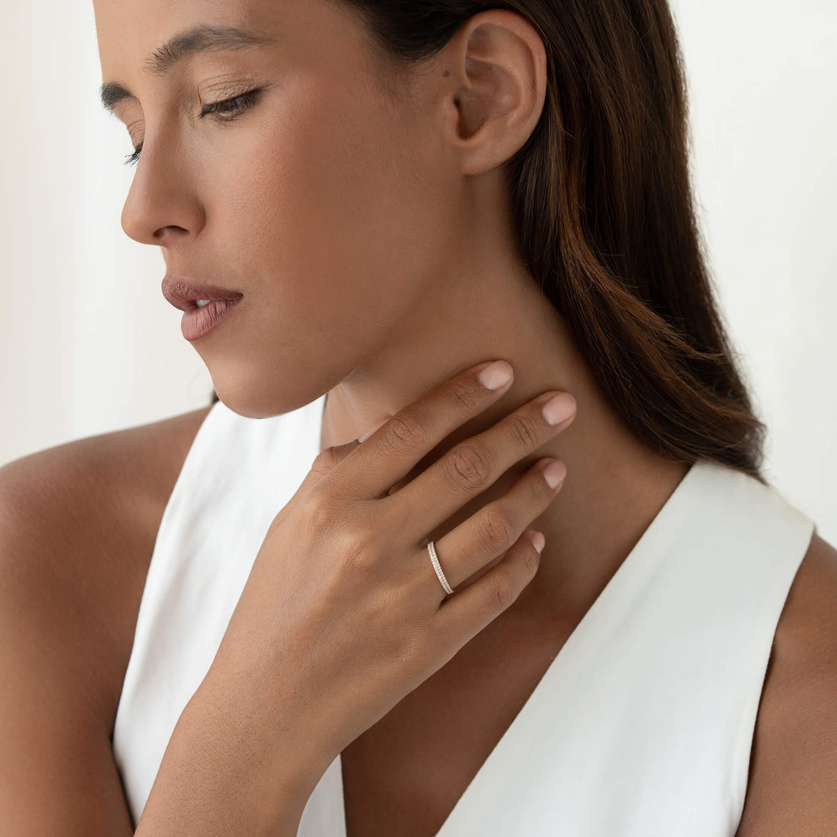 Woman in a white sleeveless top wearing a delicate Gold ring, with her hand gently resting near her neck against a clean white background.