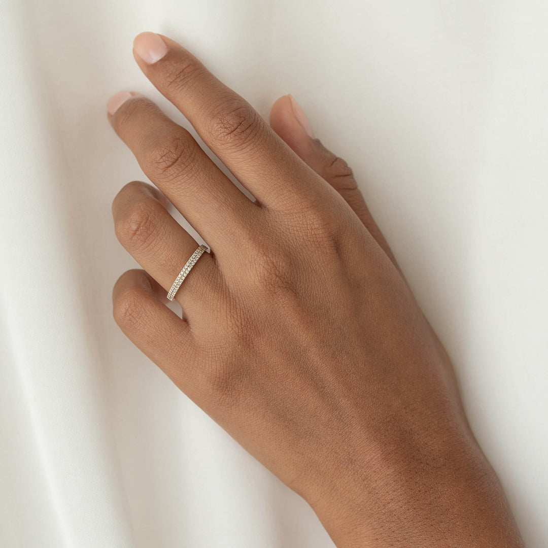 Hand wearing a delicate Gold band ring with small sparkling diamonds, resting against a soft white fabric background.