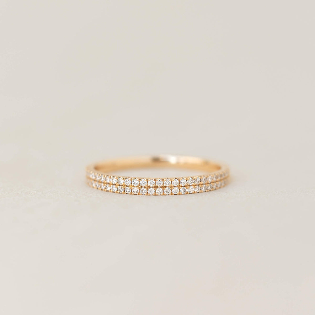 Double band half gold ring featuring small sparkling diamonds, photographed against a soft warm off-white background