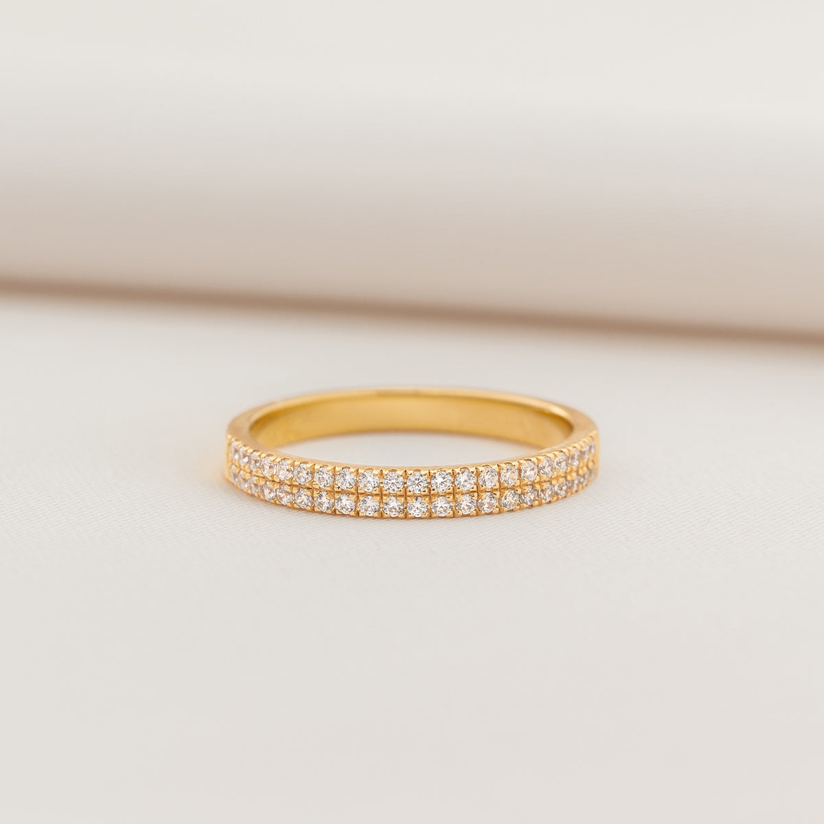 Delicate Gold band ring featuring two rows of round-cut cubic zirconia, photographed on a light neutral background.
