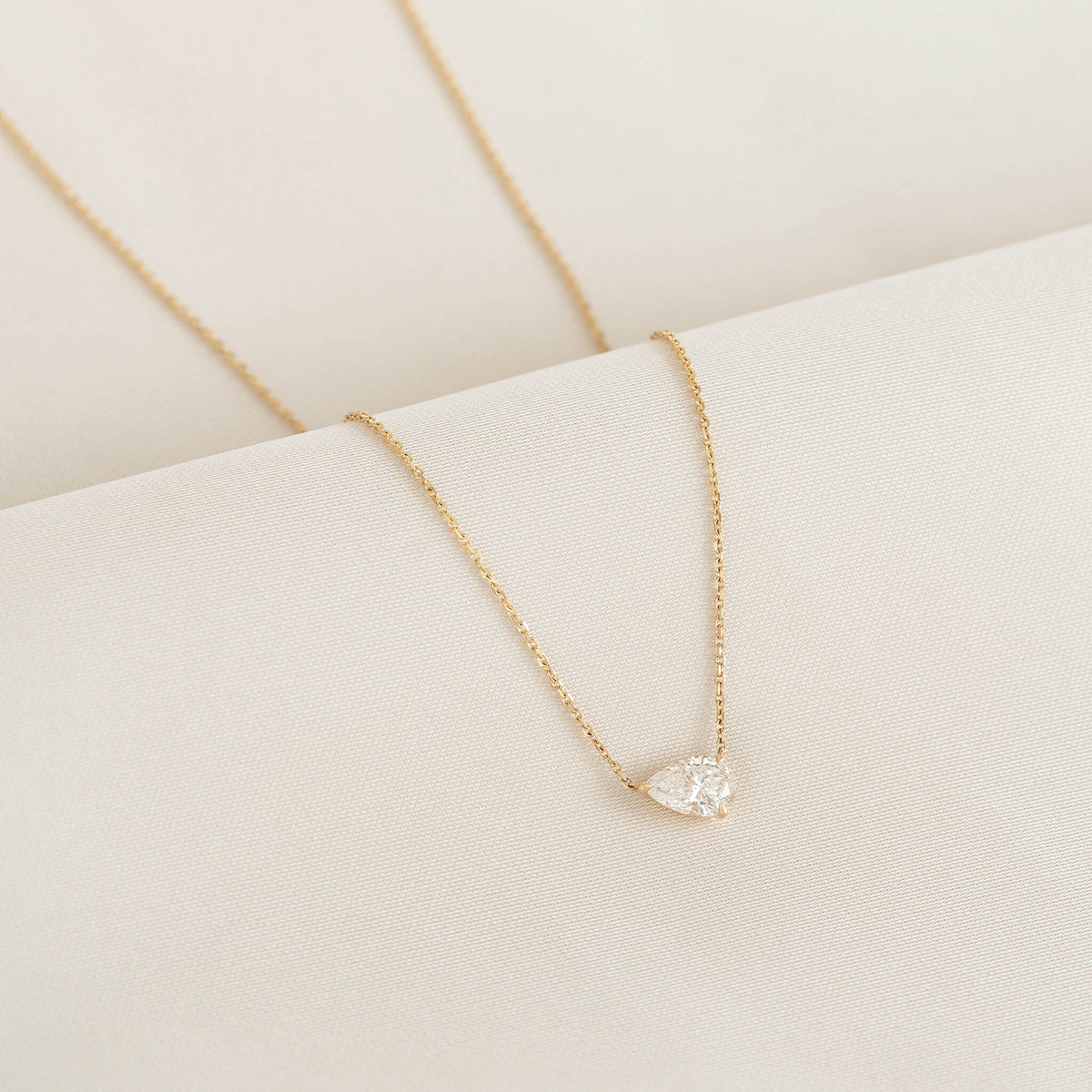Delicate Gold necklace with a pear-shaped clear gemstone pendant displayed on soft ivory fabric.