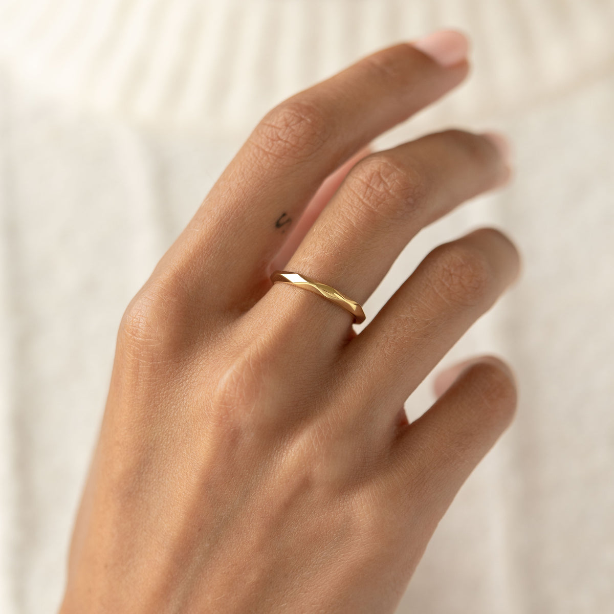 Close-up of a hand wearing a gold vermeil Faceted Ring - Rikka with a geometric wide band on a neutral background