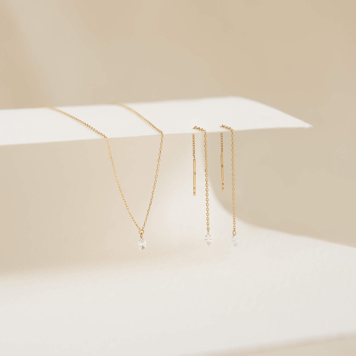 Minimalist Gold jewelry set with delicate chain necklace and dangling earrings, each adorned with small clear gems, elegantly displayed on a soft beige background.