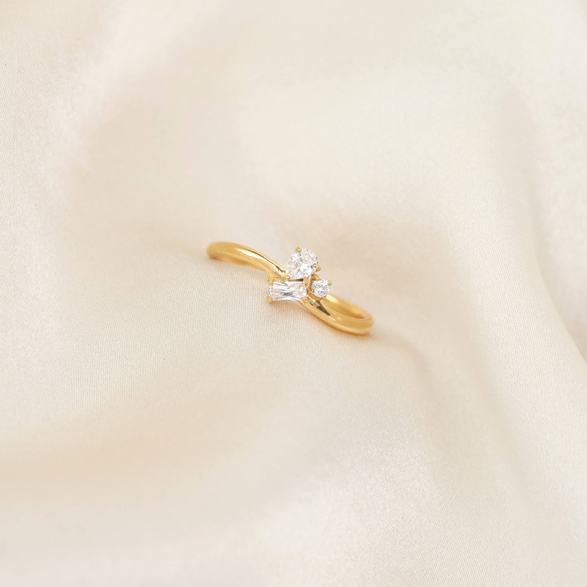 Delicate Gold Vermeil ring with a slim band, featuring a cluster of mixed-cut gemstone including pear, round, and baguette shapes, placed on softly draped ivory fabric.