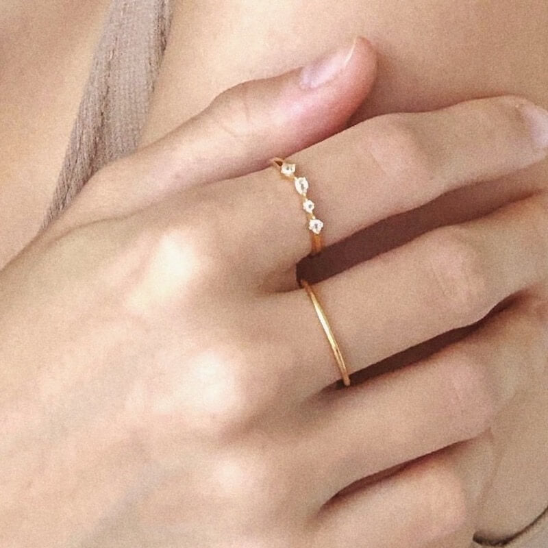 Close-up of a hand wearing two delicate gold rings, one with small diamonds and one plain, against a soft beige background