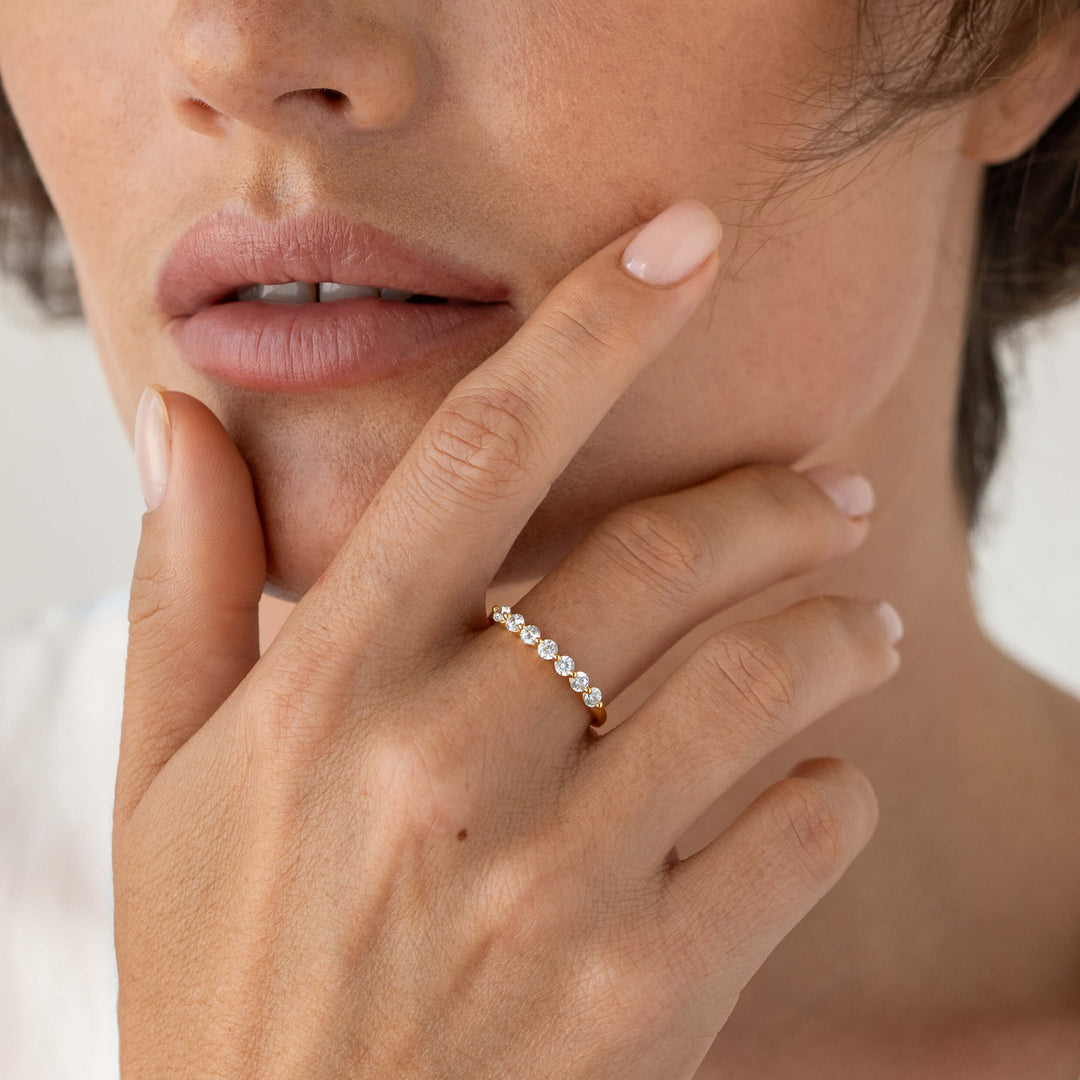 Close-up of a woman gently touching her face while wearing a delicate Gold ring set with a row of round cubic zirconia.