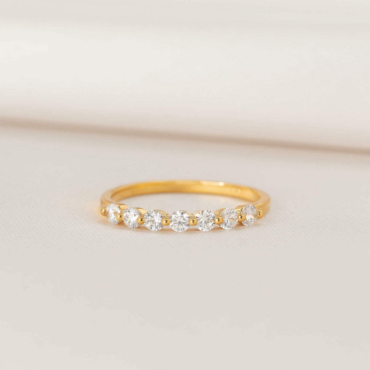 Gold ring featuring a row of round brilliant-cut cubic zirconia set across the front, photographed on a soft cream background.