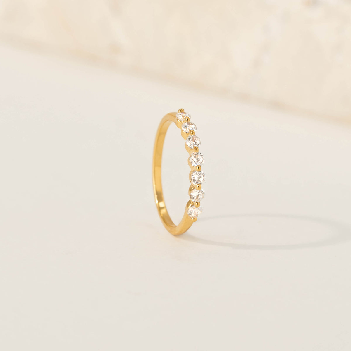 Gold ring featuring a row of round brilliant-cut cubic zirconia, standing upright on a soft cream background.