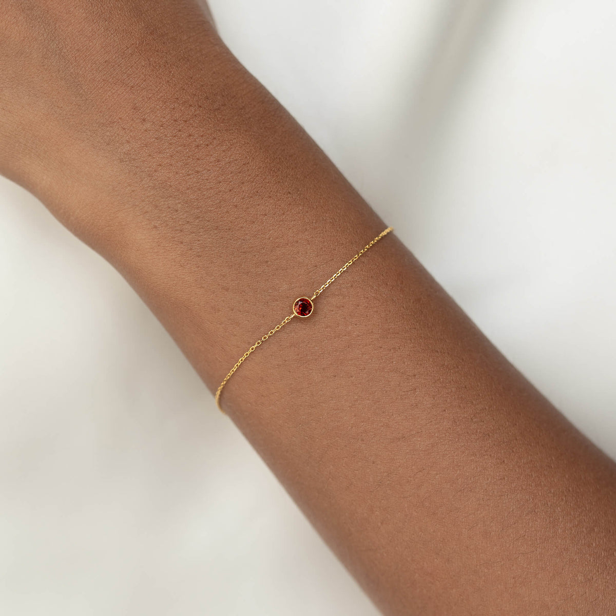 Delicate Gold Vermeil chain bracelet with a small round Garnet gemstone centerpiece, worn around a woman's wrist.